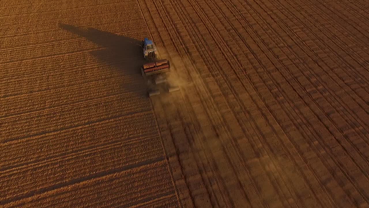 Semina campi con trattore e seminatrice in un campo polveroso, vista aerea