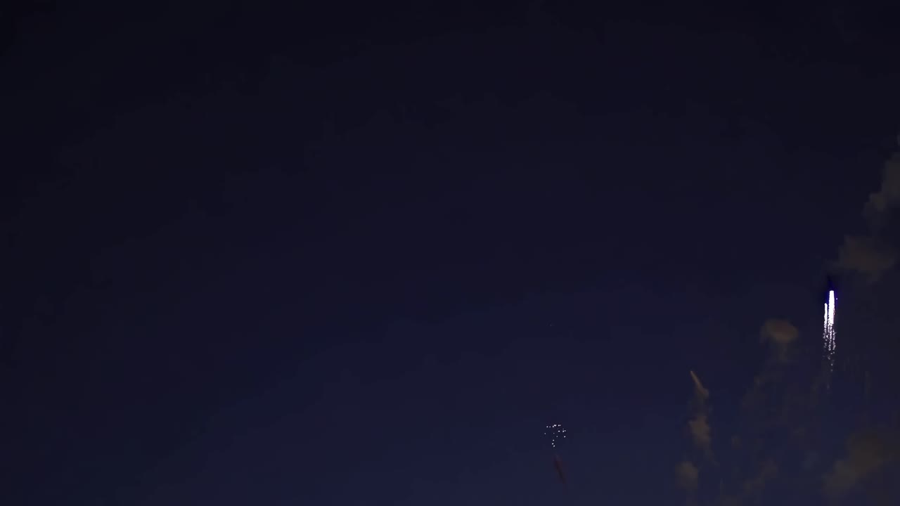 Aerial video captures a vibrant firework exploding against a dark sky, viewed from below