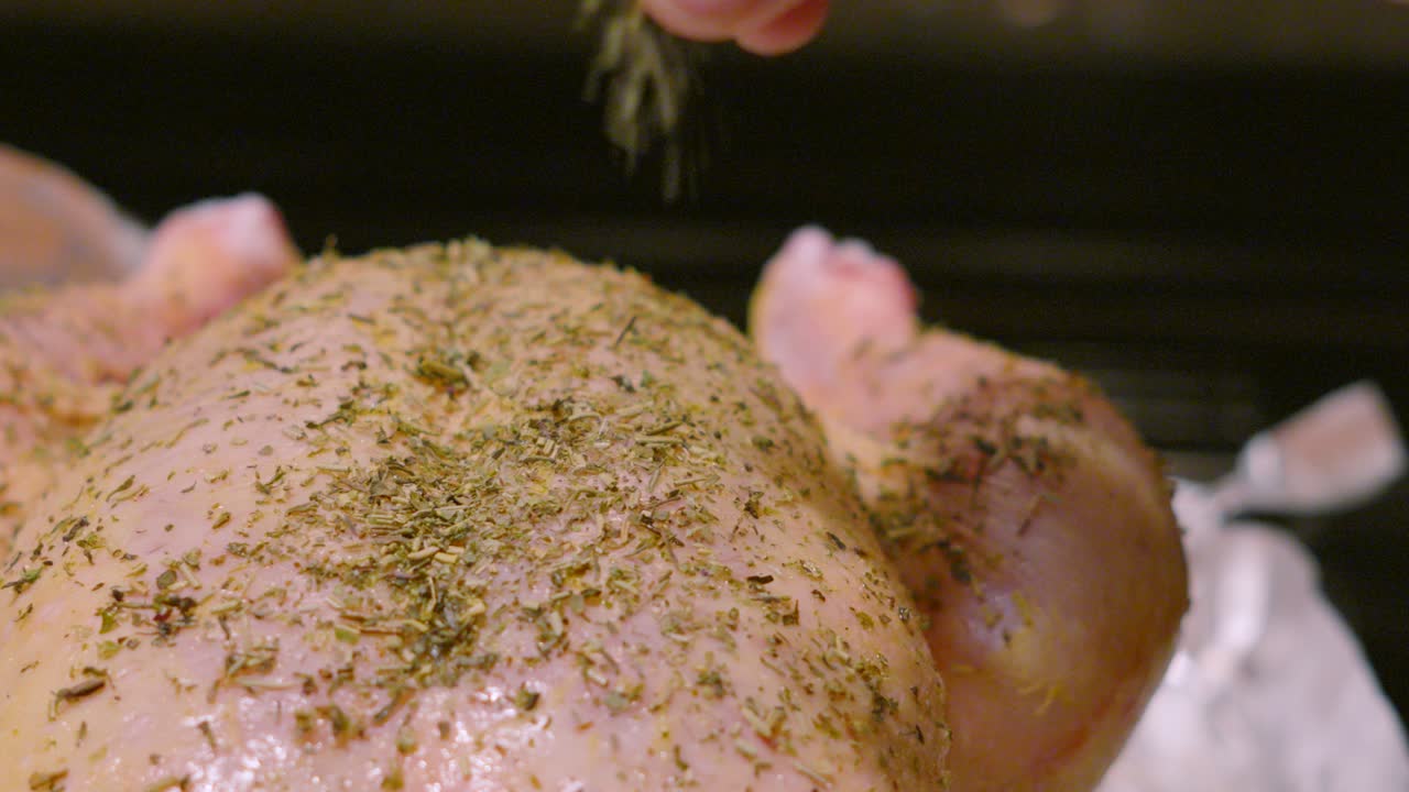 Raw Whole Free Range Chicken Being Seasoned with Herbs with Hand Dropping Ingredients in Slow Motion with Legs Visible Ready to Roast in oven After Preparing. Cooking Food Footage 4K.