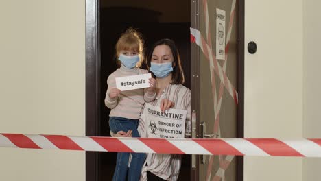 sick mother with kid daughter in medical masks opening home door, coronavirus quarantine lockdown