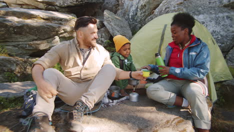 multiethnic family drinking tea at campsite