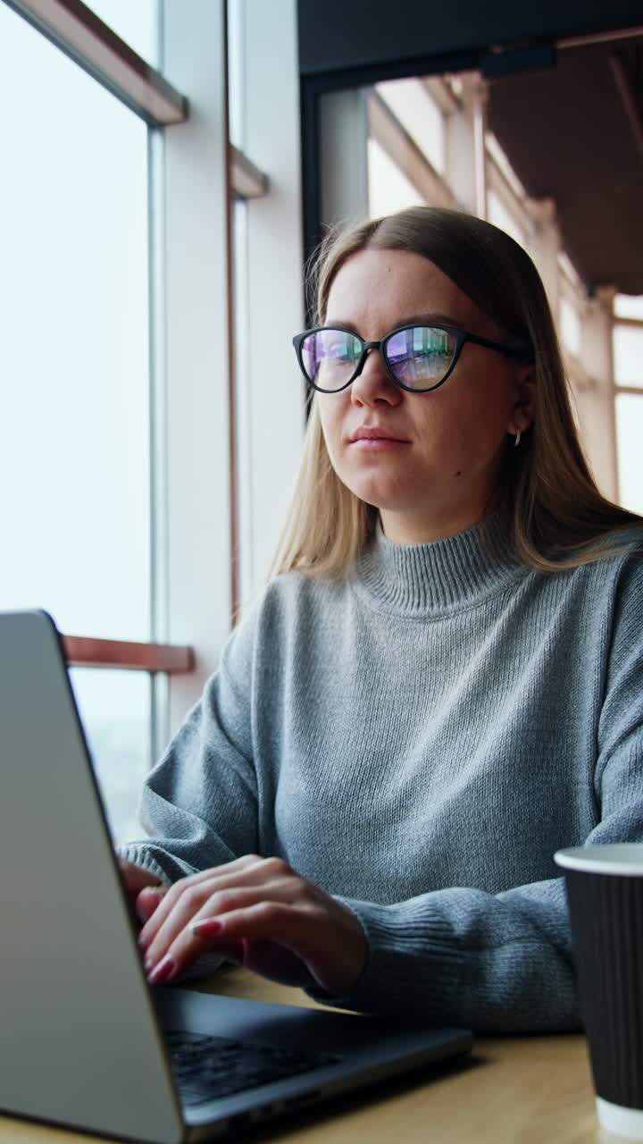 Focused young lady working on her laptop. Entrepreneur has some problem, finds a mistake and looks puzzled. Low angle view. Vertical video
