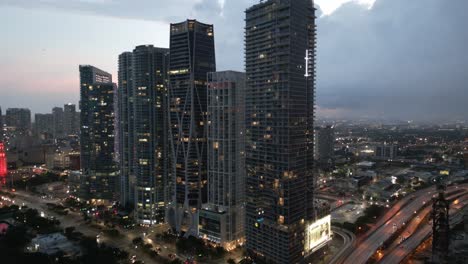 Panorámica-Aérea-Al-Atardecer-Del-Centro-De-Miami-Iluminado-Por-La-Noche-Con-Un-Moderno-Edificio-De-Rascacielos-Drone-Revela-El-Horizonte-De-La-Ciudad-Inteligente