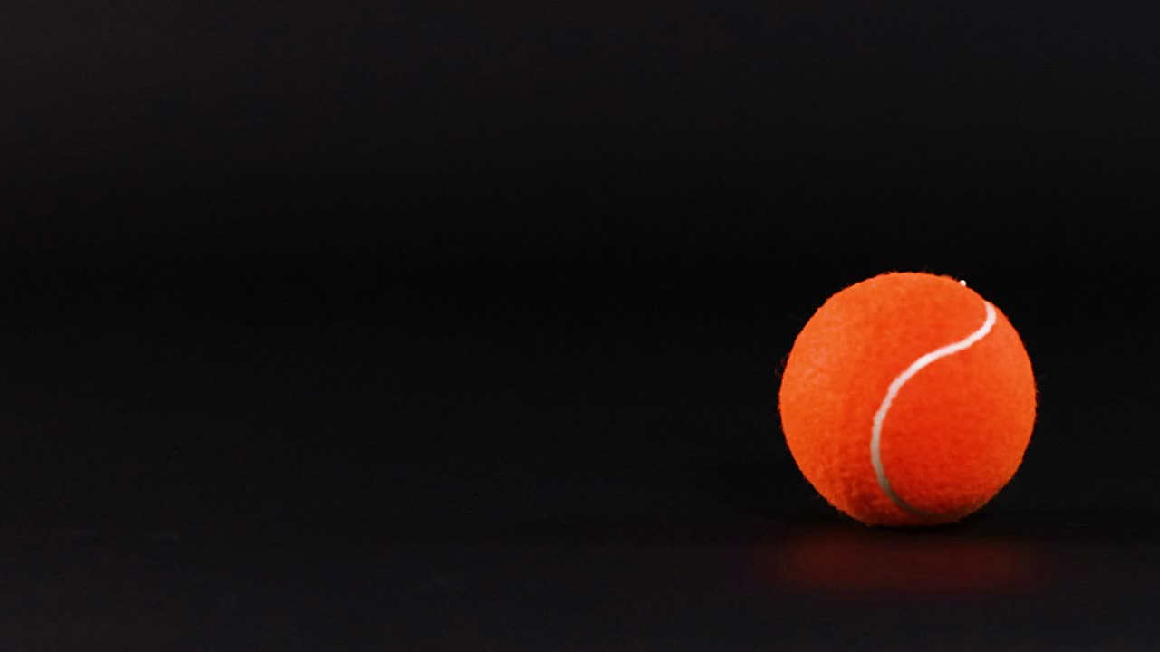 An orange tennis ball sits stationary on a dark surface, showcasing its texture and color contrast.