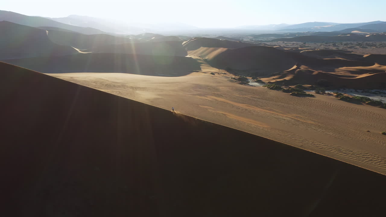 Aerial view tracking a person running up a sand dunes, sunny day in the Namib desert, Namibia