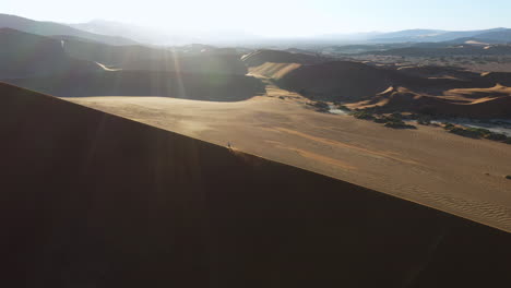 Aerial view tracking a person running up a sand dunes, sunny day in the Namib desert, Namibia
