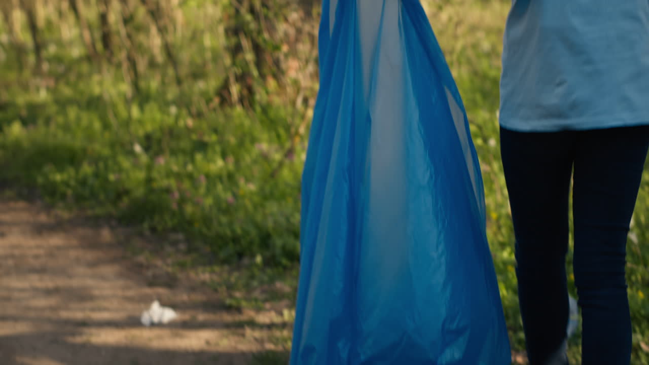 African american girl collecting rubbish in a trash bag using tongs