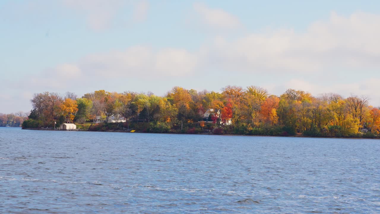 Tranquil lake surrounds a small island with autumnal trees under a blue sky in Minnetonka, Minnesota
