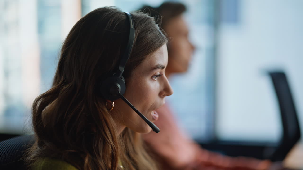 Nærbilde av kvinnelig resepsjonist med headset som ser på datamaskinen i et kundestøttekontor