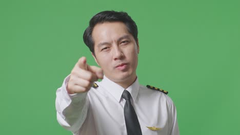 close up of asian man pilot smiling and touching his chest then pointing at you while standing in the green screen background studio