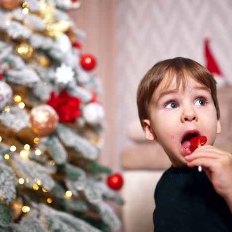 sweet little toddler boy eating a lollypop. baby boy having sweets near the christmas tree.