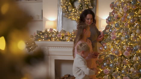 mother, little boy and girl decorate christmas tree with balls and ornaments