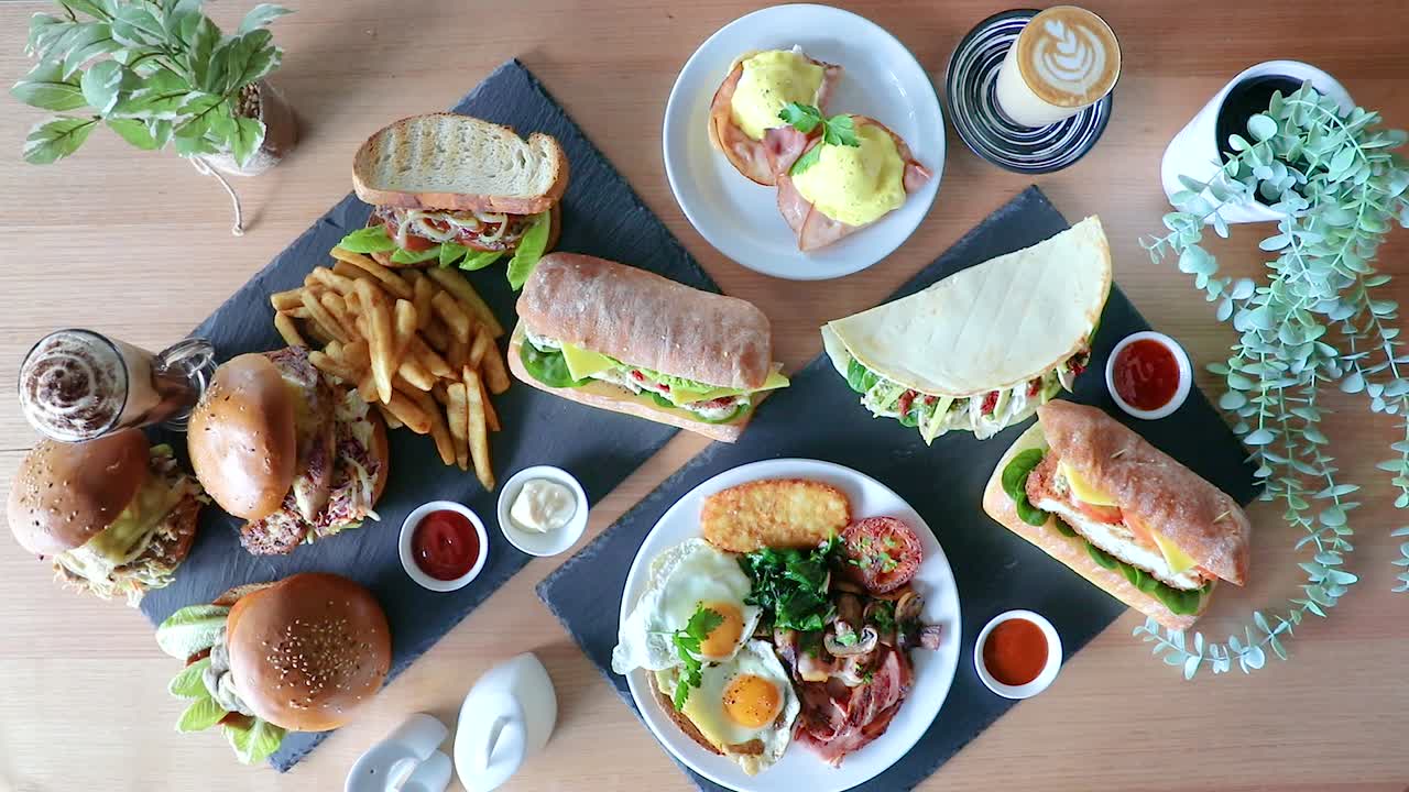 mano masculina rotando huevos benedictinos en café brunch plano con sándwiches, hamburguesas y papas fritas