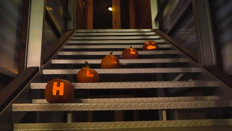 carved halloween pumpkins that have the letter hell carved into them and a scary face in top. pumpkin carvings are lit from the inside by candle light during night or evening time on a metal staircase