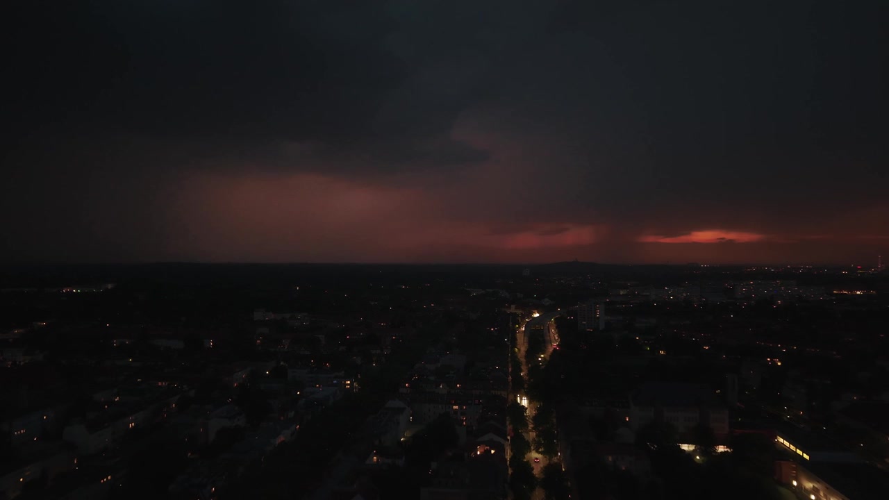 Blesky blikající nad městem v noci, osvětlující mraky a panorama s auty jedoucími po ulici během bouřky. Úžasný letecký panoramatický záběr dronem s posunem vpřed.