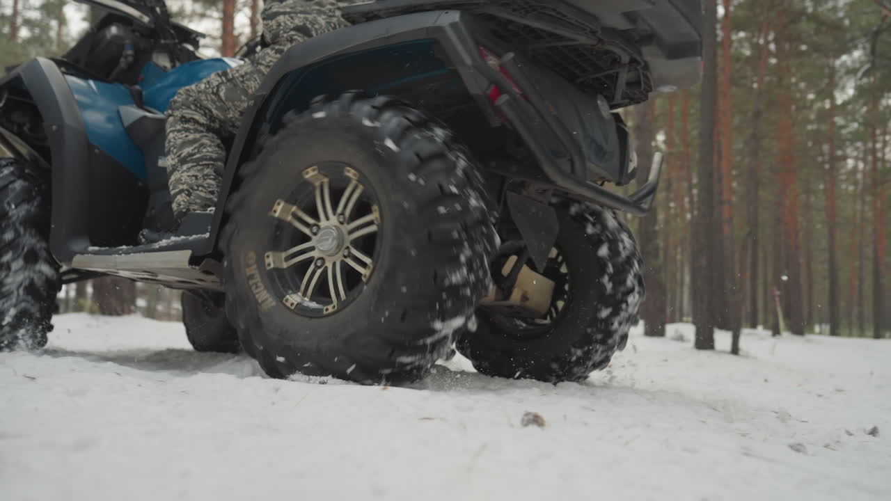 Due ATV al minimo con pneumatici maggiorati in una radura innevata di pini, primo piano sul battistrada e sulle sospensioni. Meccanici che ispezionano la trasmissione e i portapacchi, i piloti preparano i caschi. Intensa attenzione su potenza e aderenza.