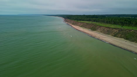a smooth shot of soft waves flowing along a coastline and a green forest landscape