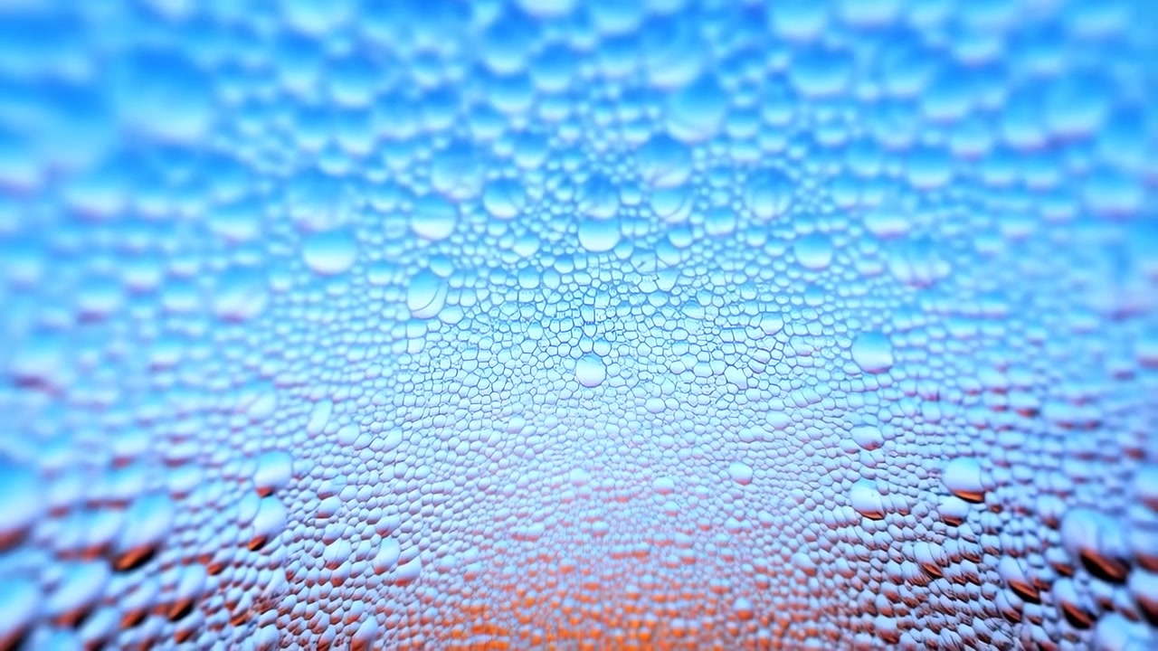 Vista dettagliata di vetro trasparente coperto da perline sparse e dense microgoccioline, che sfuma dalla luce blu fredda a quella arancione calda, creando riflessi morbidi, texture lucida, sfondo astratto.