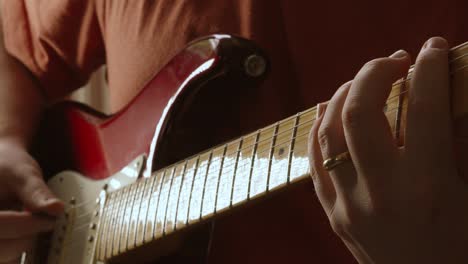 male guitarist playing various musical notes with plectrum on red electric guitar fretboard in slow motion with natural lighting 4k