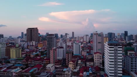 Vista-Aérea-Desde-Un-Dron-Panorámico-Hacia-La-Izquierda-Con-Vistas-A-La-Capital-De-Camboya,-Phnom-Penh,-Mientras-Se-Pone-El-Sol.