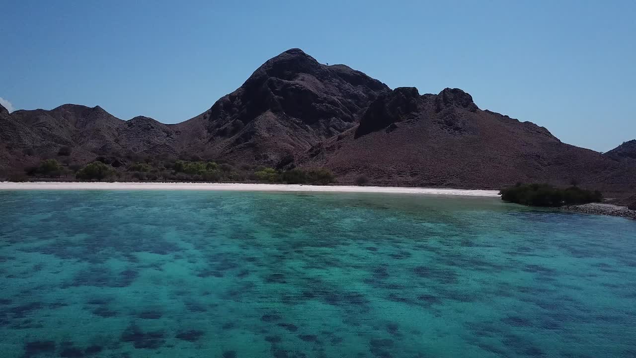 Beautiful drone shot flying closely above the blue ocean and flying upwards, showing a deserted island in West Nusa Tenggara, Indonesia