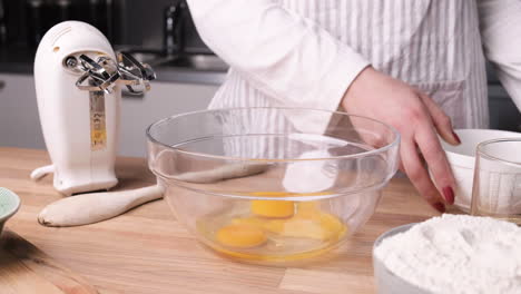 woman pouring eggs and sugar into glass bowl