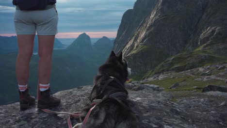 legs of hiker standing on cliff edge next to pet dog on leash at sunset