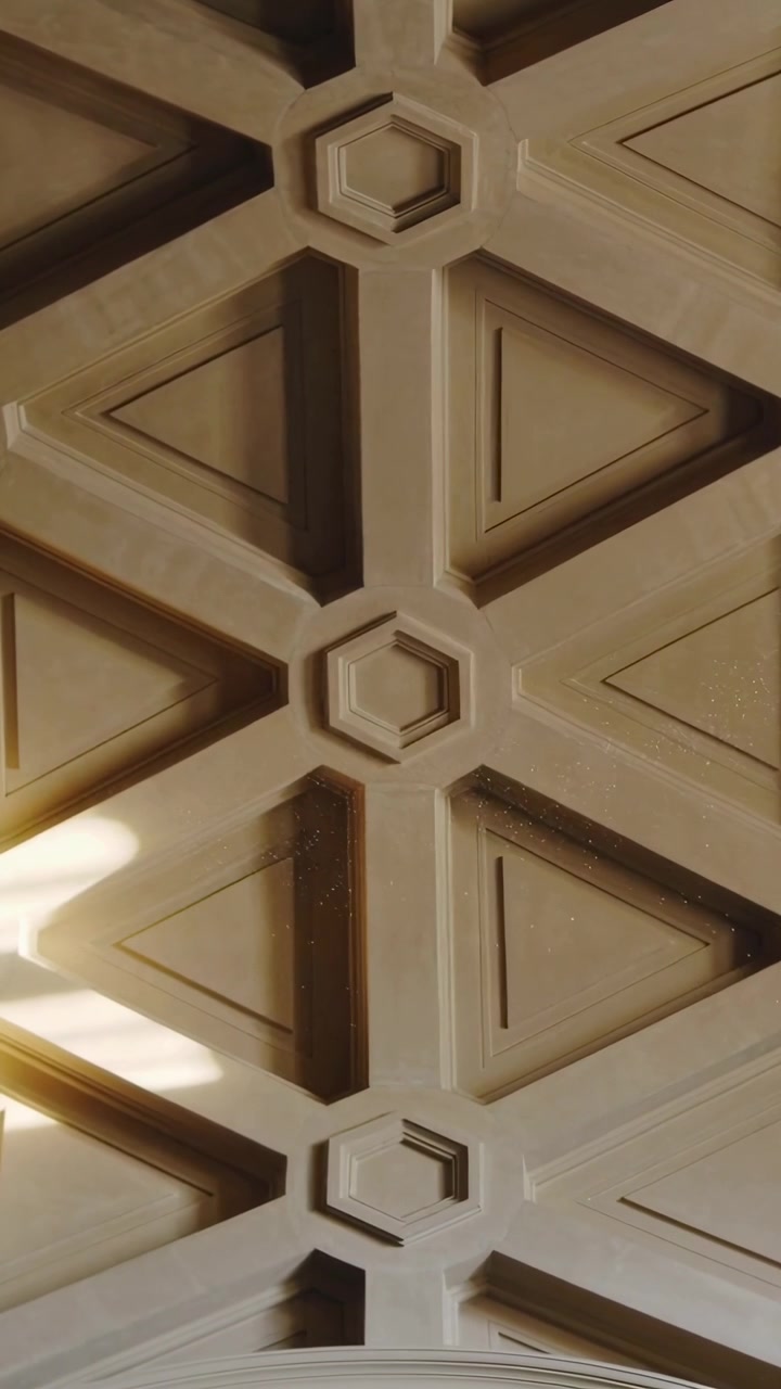 Video verticale: Inclinazione della telecamera che centra un medaglione esagonale sul soffitto di un corridoio, la luce del sole che cattura la polvere.