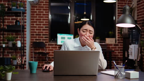 exhausted worker working overnight, typing on laptop, drinking coffee