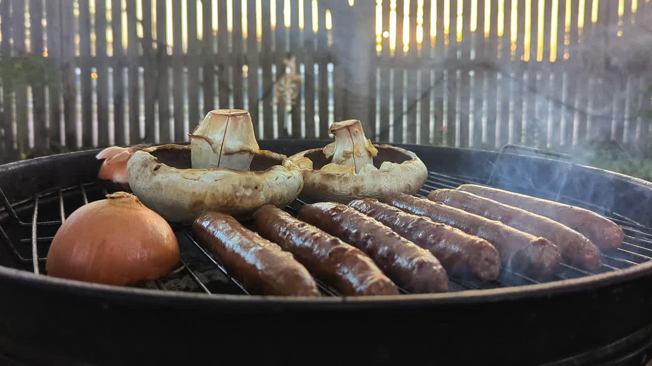 A person with tongs checks the sausages and mushrooms while grilling on the BBQ.