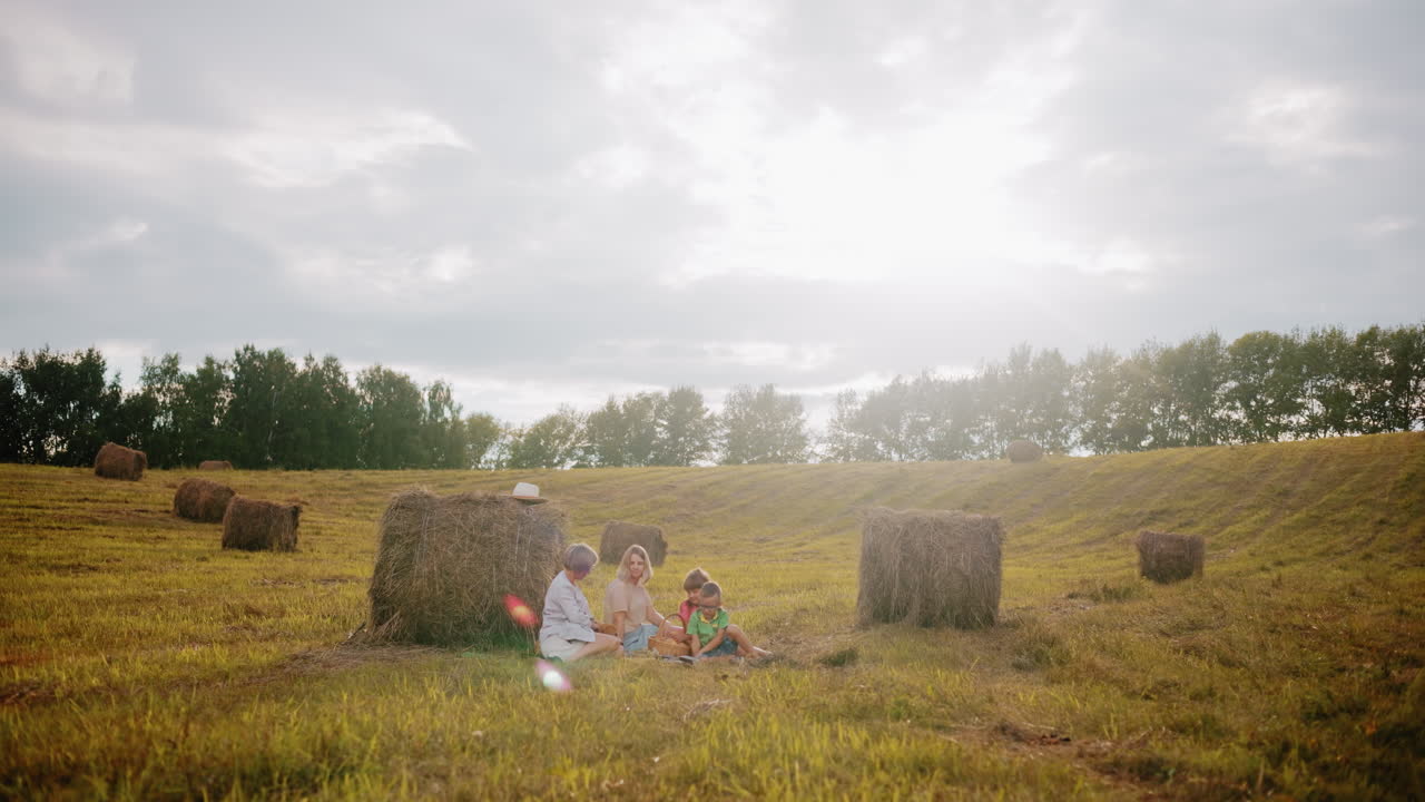 열린 시골에서 미니 피크닉을 즐기는 행복한 가족, 따뜻한 빛 빛과 카메라 플레어가 꿈 같은 분위기를 만드는 데기 사이에서 담요에 앉아