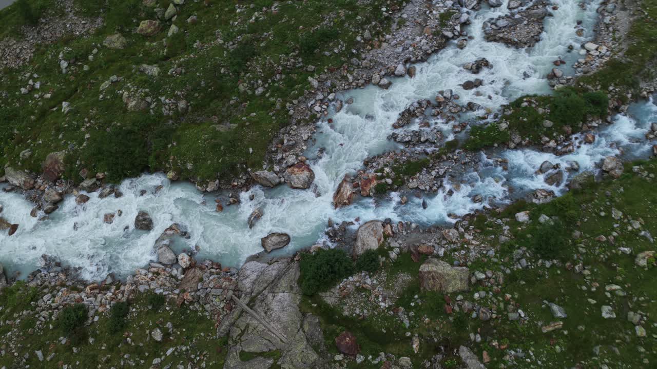 Wld river with glacial meltwater flowing over rocks, Swiss Alps. Aerial top-down descending