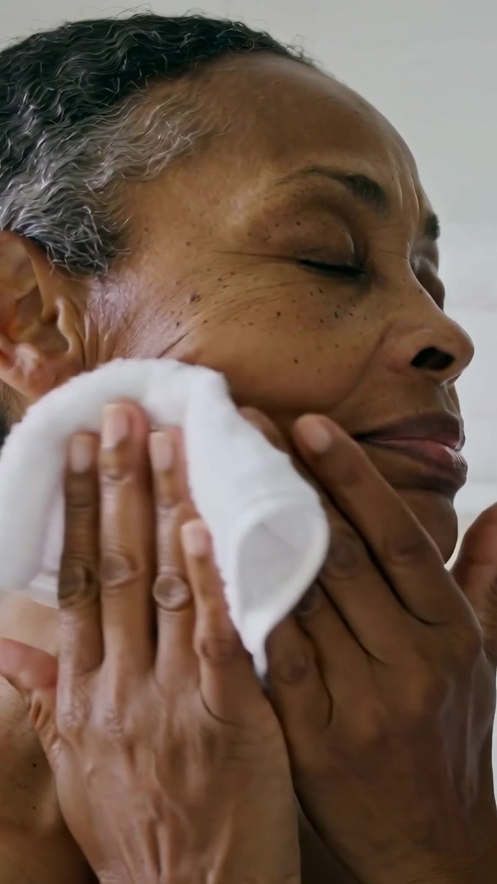 Vertical video: Wiping senior woman drying face with white towel in bath, showing bare shoulders