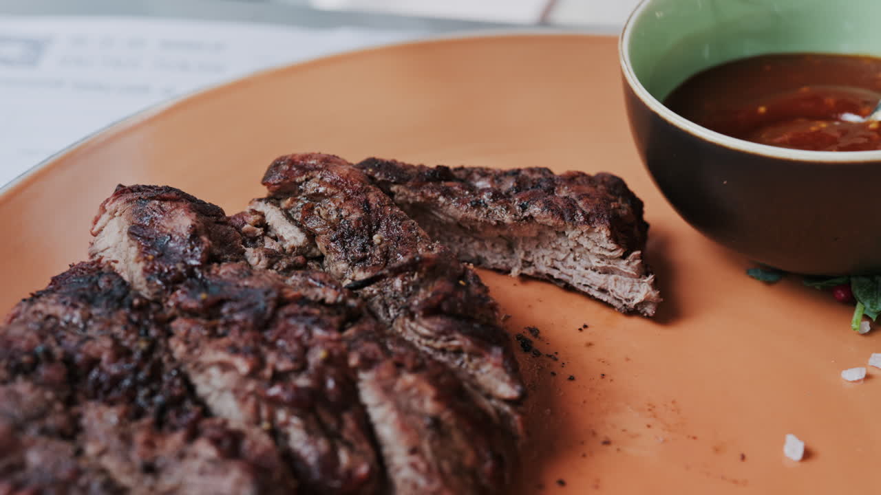 Close up of a woman's hands cutting a Sirloin Steak with Barbecue Sauce and micro-plants on the side