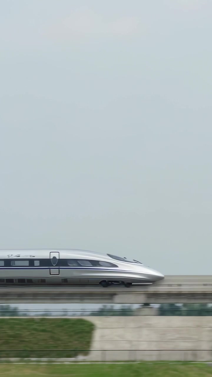 Video verticale: Treno ad alta velocità argentato che entra da sinistra, muovendosi lungo i binari sopra un pendio erboso.