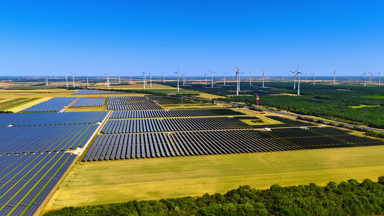 Bright skies, green energy. Aerial view of a renewable energy farm with solar panels and wind turbines under a blue sky and greenery