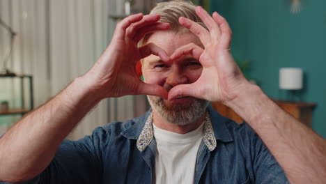 Happy-middle-aged-man-makes-symbol-of-love-showing-heart-sign-to-camera-express-romantic-feelings