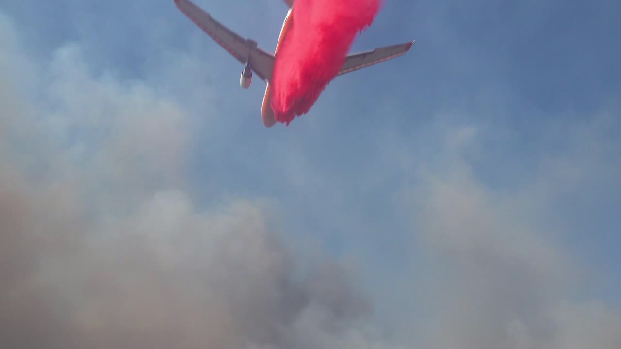 공중 유조선 항공기는 남부 캘리포니아 위의 언덕에서 타는 산불 위에 분홍색 phoschek 방화제를 떨어 뜨립니다.
