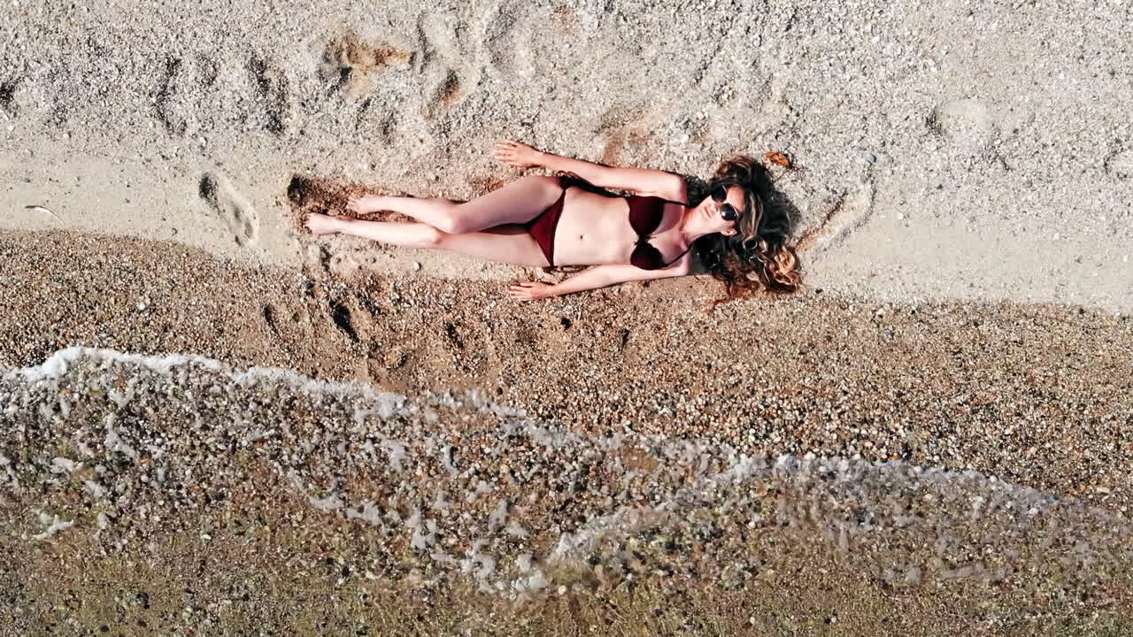 Young woman sitting on the beach sand near water and relaxing. Top view