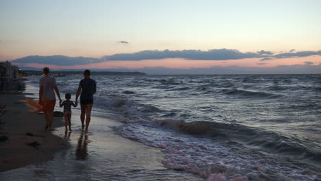 Family-of-three-walking-barefoot-along-the-shore