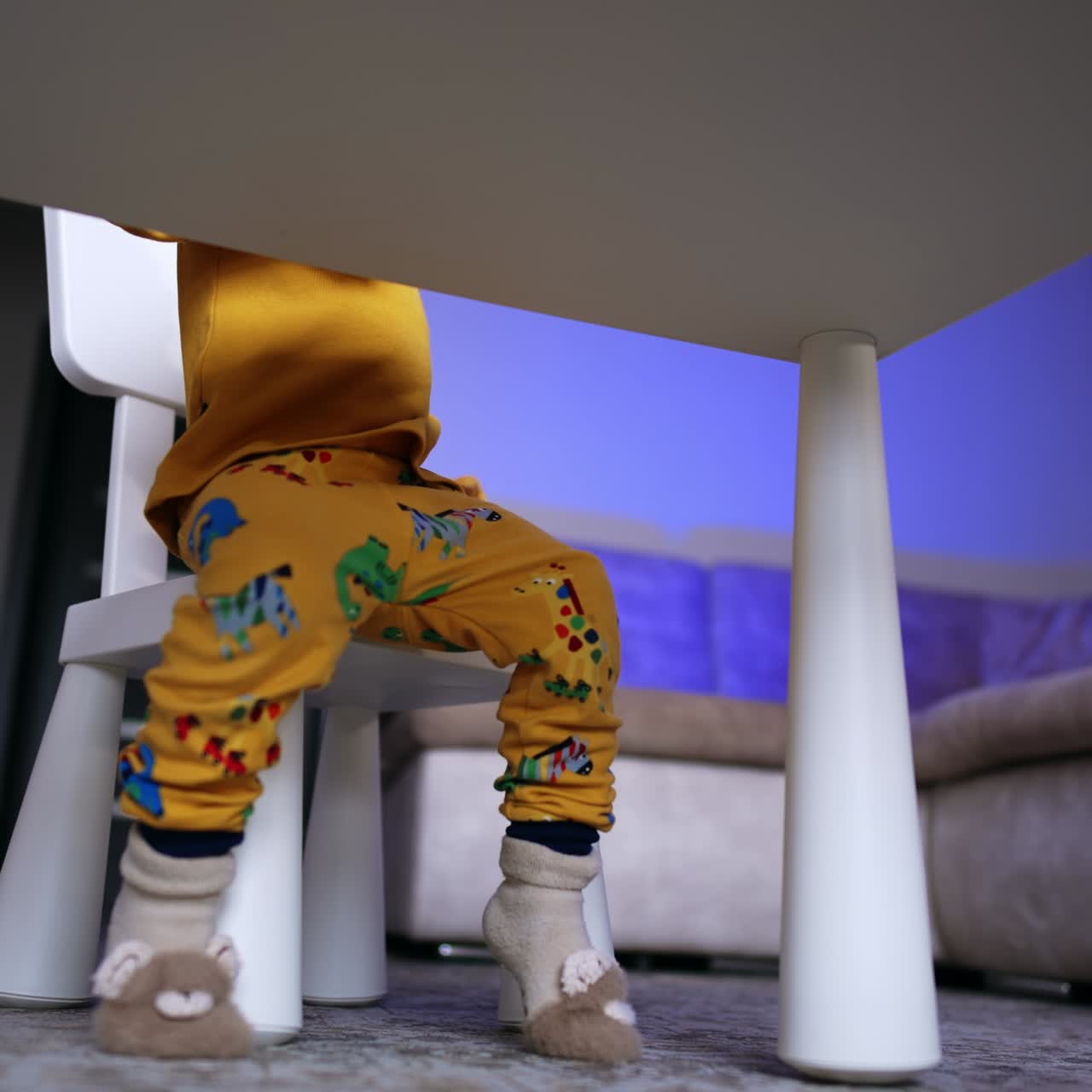 La parte inferiore del corpo di un bambino seduto alla scrivania. Un bambino mette il suo peluche sulla sedia.