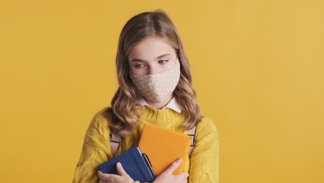 teenage caucasian girl with face mask holding books.