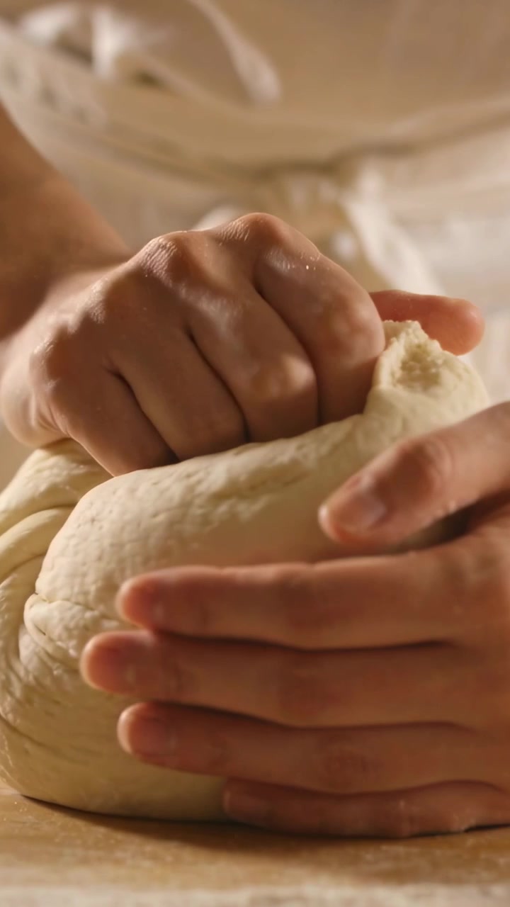 Vertical video: Shaping baker's hands after rest, forming dough into tight ball on counter in apron