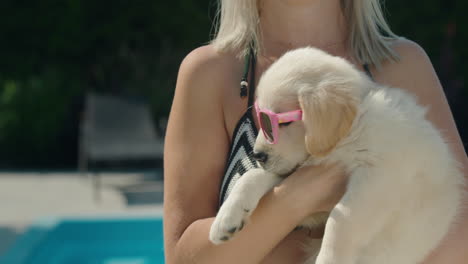 a woman in a bikini holds a blonde puppy in sunglasses in her arms. summer and vacation with a pet concept