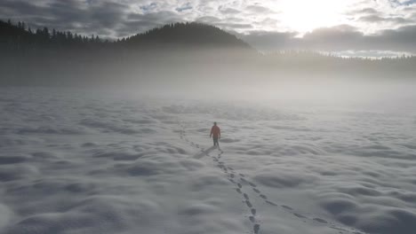 Aerial-spinning-shot-lonely-man-walking-deep-in-snow-misty-hills-winter-day