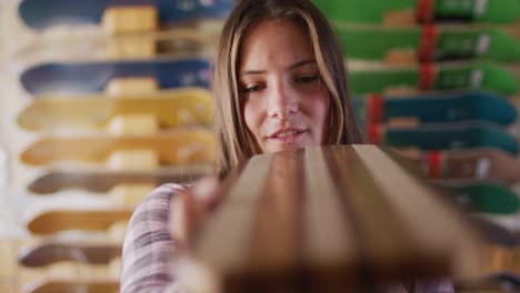 Video-Einer-Glücklichen-Kaukasischen-Skateboarderin,-Die-Skateboard-Im-Skateshop-Repariert