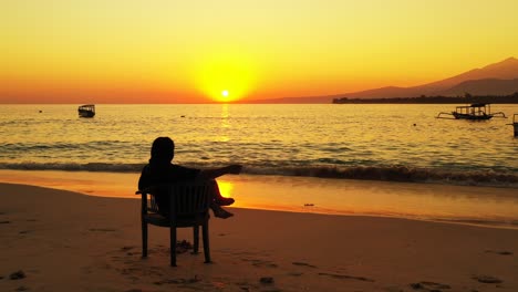 Silhouette-Einer-Frau,-Die-Sich-Während-Des-Goldenen-Sonnenuntergangs-Im-Stuhl-Am-Sandstrand-Entspannt