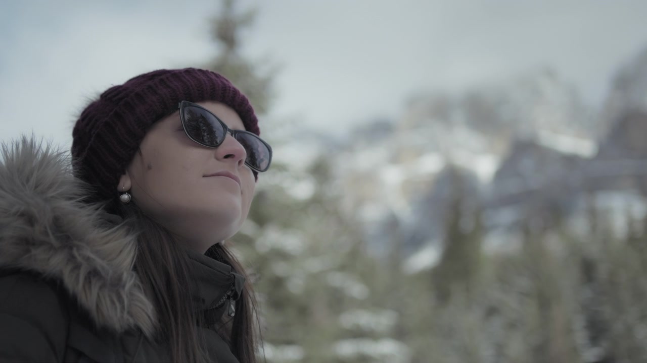 Primo piano di una donna con occhiali da sole sullo sfondo di montagne innevate in inverno