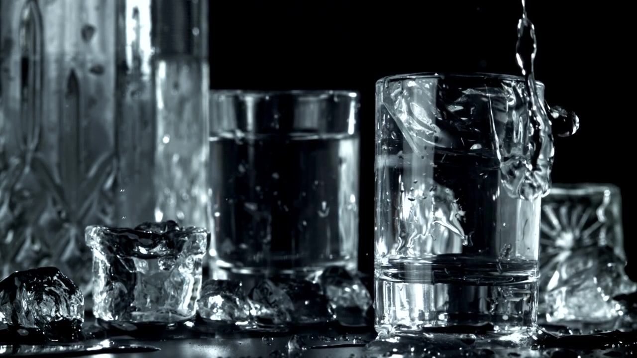 Slowmotion isterning falder ned i et shotglas med klar væske
