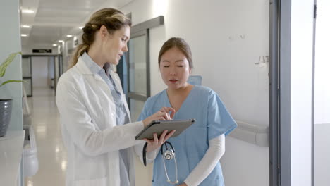 Focused-diverse-female-doctors-using-tablet-discussing-in-hospital-corridor,-slow-motion